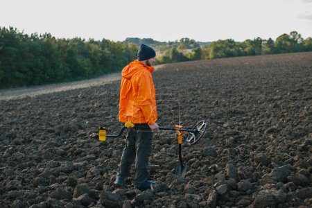 Foto de Un joven busca tesoros con un detector de metales en un campo arado. - Imagen libre de derechos