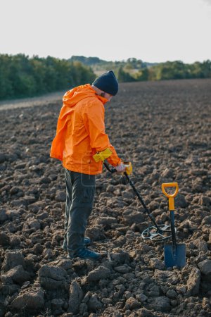 Foto de Un joven busca tesoros con un detector de metales en un campo arado. - Imagen libre de derechos