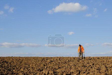 Téléchargez les photos : Un jeune homme cherche un trésor avec un détecteur de métaux dans un champ labouré. - en image libre de droit