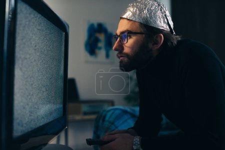 Foto de Hombre en estaño sombrero de aluminio y manta viendo la interferencia de televisión - Imagen libre de derechos