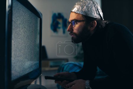 Foto de Hombre en estaño sombrero de aluminio y manta viendo la interferencia de televisión - Imagen libre de derechos