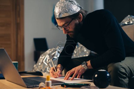 Verschwörungstheorien. Ein Mann mit weißem Hut sucht nach Zeichen, während er ein Video auf einem Laptop anschaut.