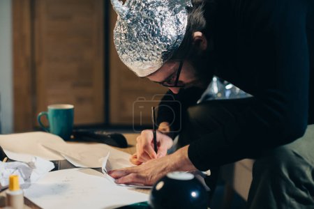 Photo for Symbolic Secrets: Man in Tin Foil Headgear Sketching Esoteric Signs - Royalty Free Image