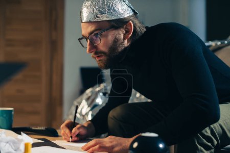 Photo for Unveiling Conspiracies: Man in Foil Hat Crafting Cryptic Signs - Royalty Free Image