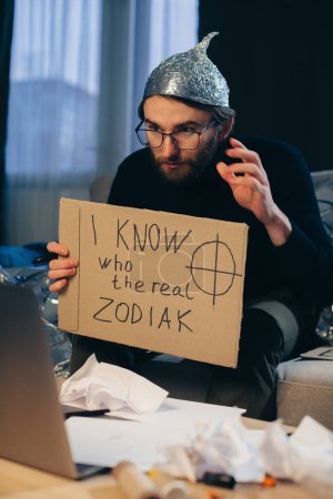 Foto de Un teórico de la conspiración en un sombrero de papel de aluminio sostiene un signo en sus manos. - Imagen libre de derechos