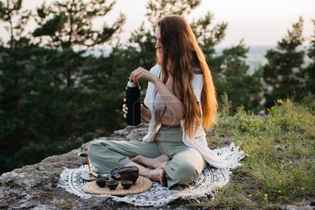 A young beautiful woman performs a Chinese tea ceremony in the mountains at sunset.