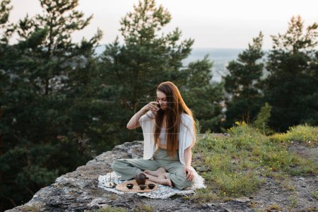 Tea ceremony in the mountains at sunset. A young woman meditates in nature.