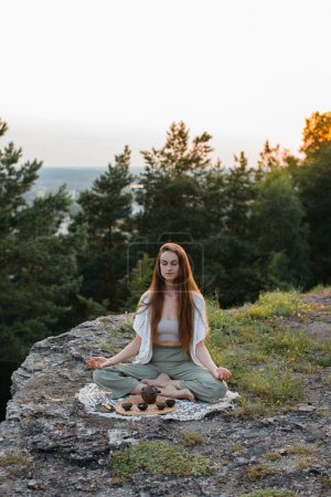 Teezeremonie in den Bergen bei Sonnenuntergang. Eine junge Frau meditiert in der Natur.