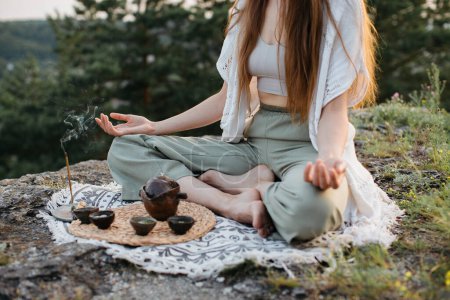 Teezeremonie in den Bergen bei Sonnenuntergang. Eine junge Frau meditiert in der Natur.