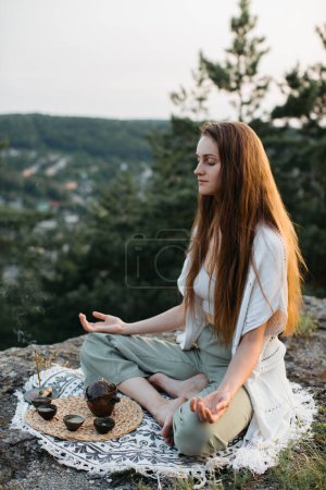 Ceremonia de té en las montañas al atardecer. Una joven medita en la naturaleza.