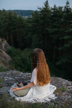 Photo for Young woman meditating using a tibetan singing bowl while sitting in a mountain landscape. - Royalty Free Image