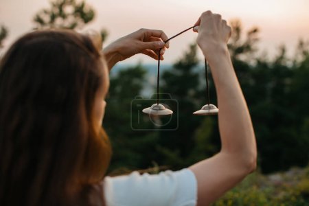 Photo for Young woman meditating with Tibetan meditation Tingsha hand bells at sunset. - Royalty Free Image