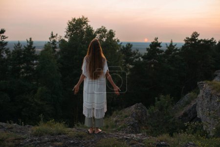 Téléchargez les photos : Le concept de loisirs et d'unité avec la nature. Une jeune femme médite dans les montagnes sur fond de soleil couchant. - en image libre de droit