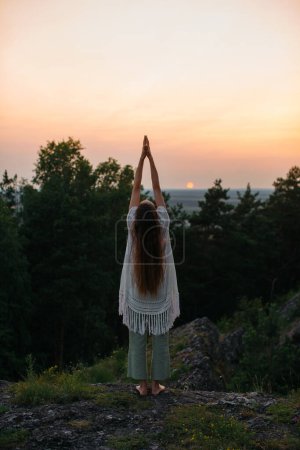 The concept of recreation and unity with nature. A young woman meditates in the mountains against the background of the setting sun.