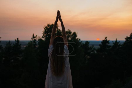 Foto de El concepto de recreación y unidad con la naturaleza. Una joven medita en las montañas sobre el fondo del sol poniente. - Imagen libre de derechos