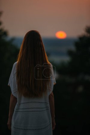 The concept of recreation and unity with nature. A young woman meditates in the mountains against the background of the setting sun.