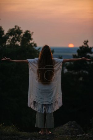 Foto de El concepto de recreación y unidad con la naturaleza. Una joven medita en las montañas sobre el fondo del sol poniente. - Imagen libre de derechos