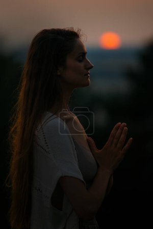 Das Konzept der Erholung und Einheit mit der Natur. Eine junge Frau meditiert in den Bergen vor dem Hintergrund der untergehenden Sonne.