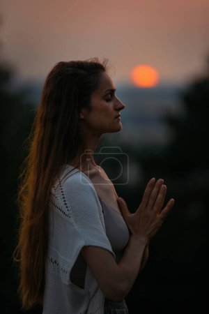 Photo for The concept of recreation and unity with nature. A young woman meditates in the mountains against the background of the setting sun. - Royalty Free Image