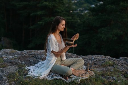 Photo for A young woman meditates with a tibetan singing bowl at sunset in the mountains. - Royalty Free Image