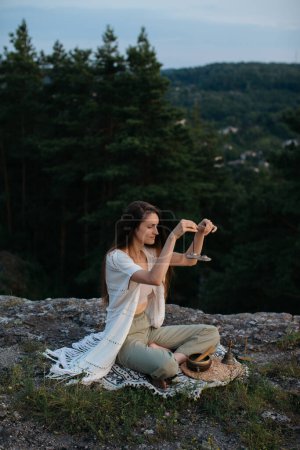 Photo for Young woman meditating with Indian Tingsha bells at sunset in the mountains. - Royalty Free Image