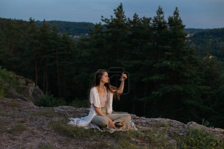 Téléchargez les photos : Une jeune femme médite avec une cloche Gantha assise sur un rocher dans les rayons du soleil couchant. - en image libre de droit
