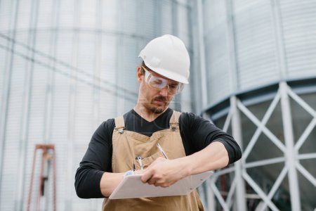Foto de Un joven ingeniero masculino en un sitio de construcción, con un sombrero duro, comprueba el estado del proyecto. - Imagen libre de derechos