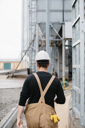 Photo for Rear view of an engineer in a hard hat and overalls at a grain silo construction site. - Royalty Free Image
