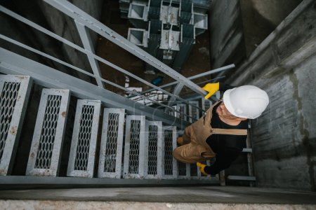 Foto de Vista superior del trabajador de fábrica subiendo escaleras de metal en el edificio del silo industrial - Imagen libre de derechos
