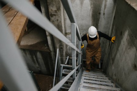 Foto de Un ingeniero de construcción sube una escalera de metal en el sitio de construcción de un silo de grano. - Imagen libre de derechos
