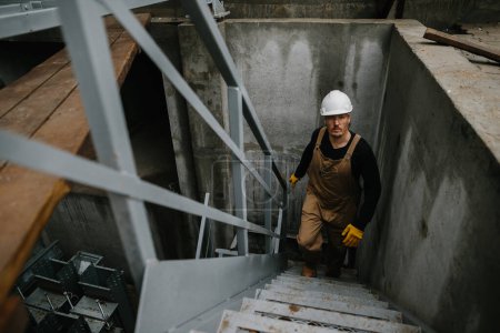 Téléchargez les photos : Un ingénieur en construction monte une échelle métallique sur le chantier d'un silo à grains. - en image libre de droit