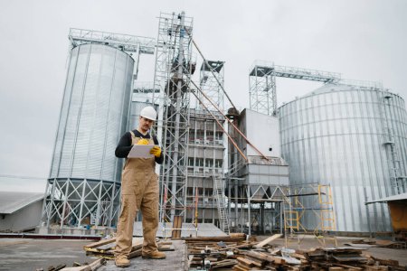 Foto de Ingeniero, trabajador industrial frente a silos llenos de grano. - Imagen libre de derechos