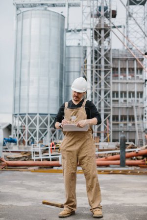 Photo for Engineer, industrial worker in front of silos full of grain. - Royalty Free Image