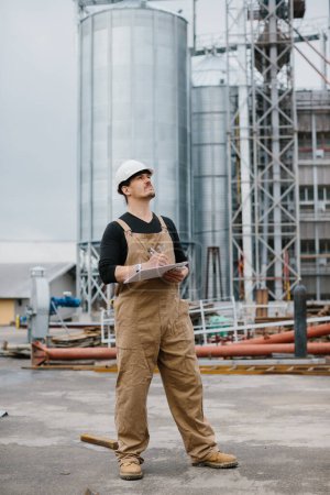 Photo for Engineer, industrial worker in front of silos full of grain. - Royalty Free Image