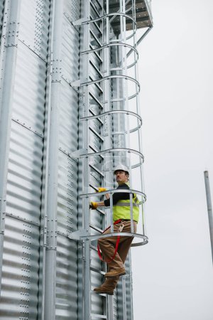 Téléchargez les photos : Un ingénieur en construction monte une échelle sur un silo à grains pour surveiller l'état de la construction. - en image libre de droit