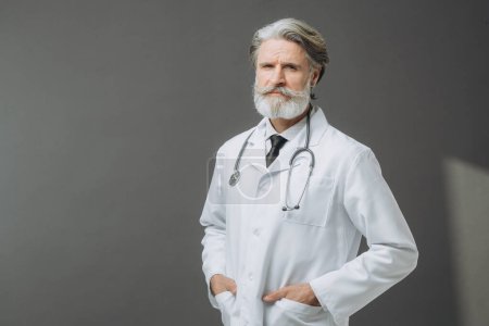 Photo for Gray-haired male doctor in a white medical coat with a phallendoscope on a gray background. - Royalty Free Image
