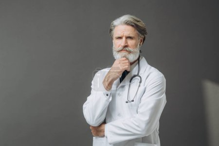 Photo for Gray-haired male doctor in a white medical coat with a phallendoscope on a gray background. - Royalty Free Image
