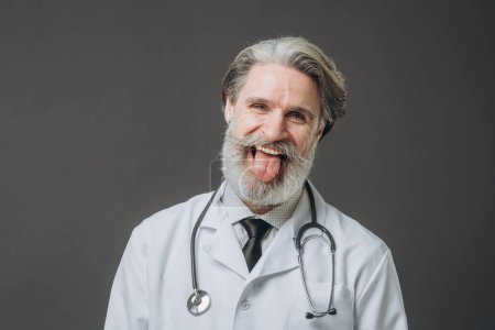 Photo for Elderly male doctor shows his tongue looking at the camera. - Royalty Free Image
