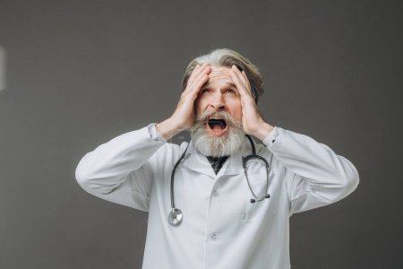 Photo for Gray-haired male doctor holding his head with a confused expression. - Royalty Free Image