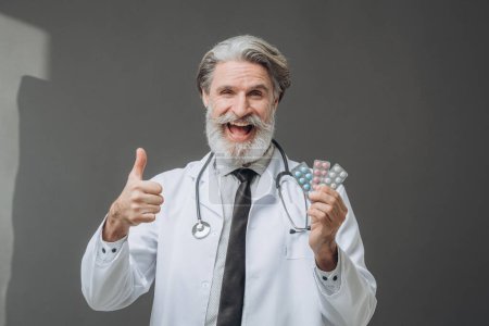 Foto de Un hombre con un abrigo médico blanco está mostrando pastillas a la cámara y sosteniendo un pulgar hacia arriba. - Imagen libre de derechos