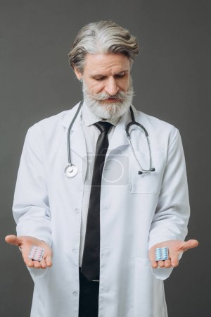 Photo for A man in a white medical coat shows pills to the camera. Red and blue pills in hands, choice. - Royalty Free Image