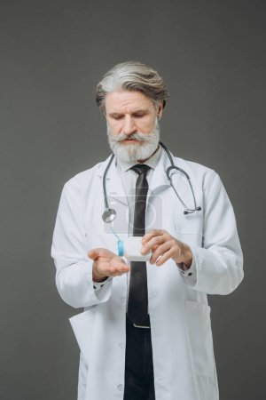 Photo for Portrait of a senior doctor pouring pills from a bottle onto his hand. - Royalty Free Image