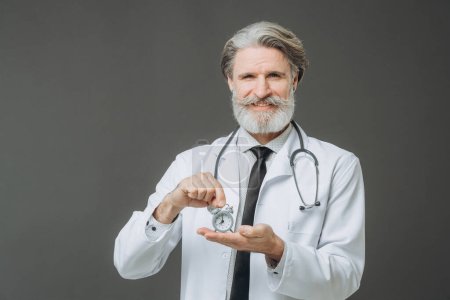 Téléchargez les photos : Portrait of a senior doctor with an alarm clock in his hands. The concept of healthcare and medicine. - en image libre de droit