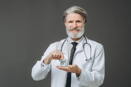 Foto de Retrato de un médico veterano con un despertador en las manos. Concepto de salud y medicina. - Imagen libre de derechos