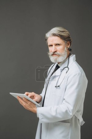 Photo for A senior doctor with a tablet in his hands. The concept of healthcare and medicine. - Royalty Free Image