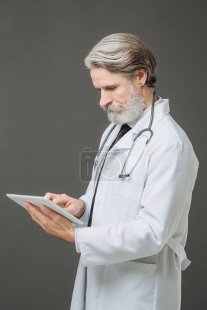 Photo for A senior doctor with a tablet in his hands. The concept of healthcare and medicine. - Royalty Free Image