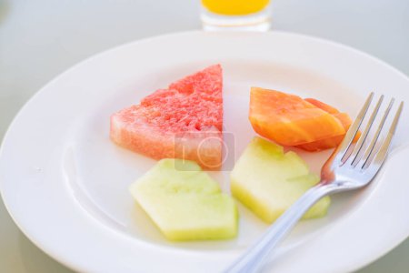 Ein weißer Teller mit Gabel und verschiedenen Fruchtscheiben, darunter Wassermelone, Papaya und Melone.