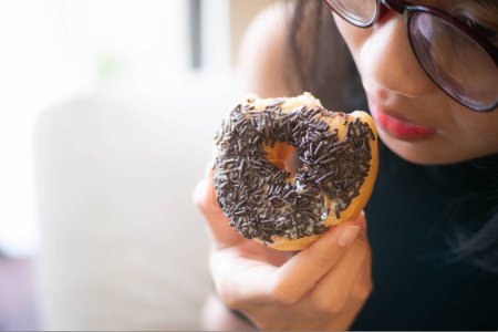 Close-up of a person holding and about to eat a chocolate-sprinkled donut.