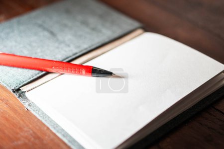 Un cuaderno abierto con páginas en blanco y un bolígrafo rojo apoyado en él, colocado sobre una superficie de madera.