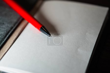 Un cuaderno abierto con páginas en blanco y un bolígrafo rojo apoyado en él, colocado sobre una superficie de madera.